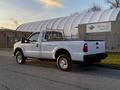 A white 2012 Ford F-250 pick-up truck with a flatbed and a metallic grille parked on a paved surface