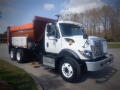 A white 2016 International WorkStar 7500 truck with an orange dump bed and black tires parked on a paved area