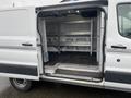 A 2018 Ford Transit van with open rear doors showing a spacious cargo area featuring metal shelving and a flat floor