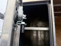 Close-up of a latch mechanism attached to a silver metal surface with visible screws and a cylindrical part inside a compartment