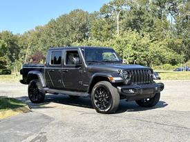 A black 2021 Jeep Gladiator with large black wheels and a rugged design is parked at an angle showcasing its front and side features