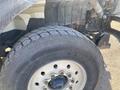 Close-up of a large tire mounted on a truck axle with a rugged tread pattern and a shiny metal wheel showing multiple bolts and a central hub