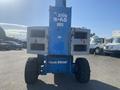 A blue 1997 Genie S-65 4X4 lift with a tall boom and large tires facing forward showing signs of wear and rust