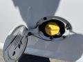A 2012 Chevrolet Express fuel cap door is open revealing a yellow fuel cap with instructions for tightening and a note about the engine light
