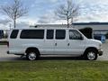 A white 2014 Ford Econoline van with multiple windows and sliding side doors parked on grass