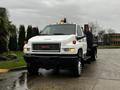 A white 2005 GMC C5 Duramax truck with a flatbed and orange roof lights parked on a wet surface