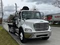 A 2006 Freightliner M2 112 truck with a flatbed and hydraulic lift system in the foreground