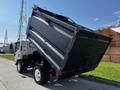 A 2016 Isuzu NPR dump truck with its bed raised for unloading material