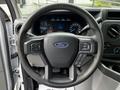 A black steering wheel with buttons and the Ford logo at the center in a 2021 Ford E-450 vehicle interior