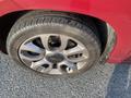 Close-up of a tire of a red 2015 Fiat 500L showing a silver alloy wheel with five spokes and visible tread pattern on the tire