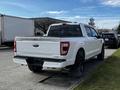 A white 2021 Ford F-150 pickup truck parked on the side of the street showing its rear and distinctive tailgate design