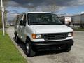 A white 2004 Ford Econoline van parked on a street with black bumpers and large tires visible in the foreground