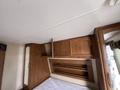 Interior view of a 2013 Outdoor Wind River showing wooden cabinetry and a section of a bed with a white mattress