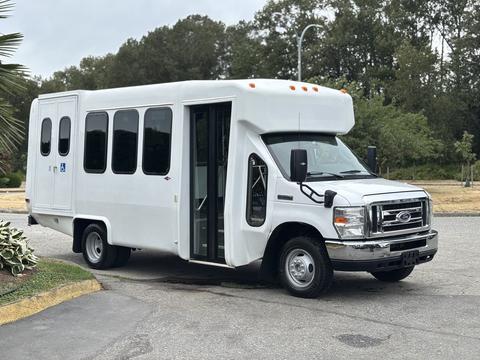 A 2014 Ford E-350 shuttle bus with a white exterior features large side windows a wide entry door and a low floor for accessibility