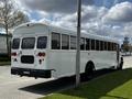 A white 2022 Blue Bird BB Conventional bus with large windows and rear lights parked beside a street