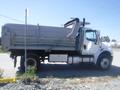 A white 2005 Freightliner M2 106 Medium Duty truck with a large dump bed parked while facing left