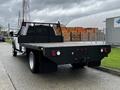 A 2017 Ford F-550 flatbed truck with a black bed and rear lights stands parked on a road with a utility trailer hitch attached