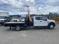 A 2017 Ford F-550 flatbed truck with a raised hydraulic arm on the side parked in an outdoor area