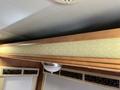 Close-up of a wooden shelf with a textured light-colored panel and a ceiling light fixture in a motorhome interior