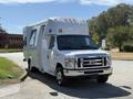 A 2013 Ford Econoline camper van in white with orange lights on the roof parked at an angle with a slide-out section extended