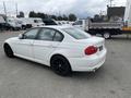 A white 2011 BMW 3-Series sedan with dark alloy wheels is parked with a slightly angled view showing its rear and side profiles