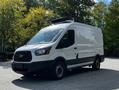 A 2015 Ford Transit van with a white exterior and a roof-mounted unit is parked prominently with a black front grille and side mirrors
