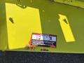 A warning label on a yellow machinery component with symbols indicating danger from discharge and moving parts