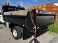 A 2021 Ford F-550 truck with a flatbed featuring wooden planks and a black bed liner with reflective lights and a chain securing the bed