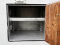 An open storage compartment of a 2005 Freightliner M2 106 featuring a single shelf and a wooden door on the right side