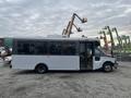 A white 2017 Chevrolet Express shuttle bus with large windows and a door on the side is parked on gravel