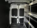 A 2021 Ford Transit van interior featuring a spacious cargo area with two large rear doors and metal shelving on one side