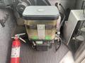 A 2012 Ford Econoline's fluid reservoir with a transparent container displaying labels and a black lid is positioned on the floor next to a fire extinguisher