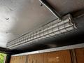 A metal fluorescent light fixture with a wire guard mounted on a ceiling in a commercial vehicle