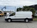A 2023 Ford Transit van in white with black trim and a roof rack parked with the side view facing the camera