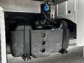 A black fuel tank mounted on the frame of a 2011 Ford F-550 with visible hoses and connectors