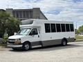 A white 2020 Chevrolet Express bus with tinted windows and a gray panel on the lower half parked on a street