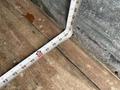 A measuring tape laid out in an L shape on a wooden surface with numbers clearly visible indicating measurements