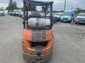 A red and black 2010 Toyota 7FGGU25 forklift with a worn exterior and a propane tank mounted on the back
