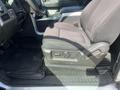 A black fabric driver's seat in a 2014 Ford F-150 with adjustable controls on the side and a rubber floor mat underneath