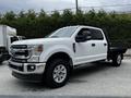 A white 2020 Ford F-350 Super Duty pickup truck with a flatbed configuration and chrome grille parked in a lot