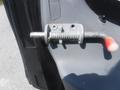 A metal latch mechanism with a coiled spring and a red handle mounted on the side of a vehicle door