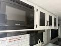 A black built-in microwave mounted above white cabinets in a kitchen area with mesh cabinet doors and a stainless steel sink below