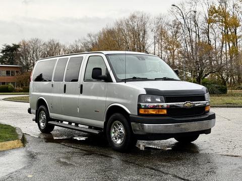A silver 2021 Chevrolet Express van parked on a wet street featuring large windows and chrome wheels