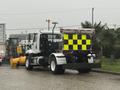 A 2016 Freightliner 108SD truck with a bright yellow and black reflective rear panel is parked with a snow plow attached at the front