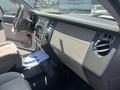 Interior dashboard of a 2013 Ford Expedition featuring control knobs air vents and a gear shift with light beige upholstery and a dark carpet floor