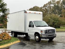 A 2013 Ford Econoline truck with a white box cargo area parked at an angle on a wet road