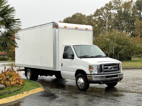A 2013 Ford Econoline truck with a white box cargo area parked at an angle on a wet road