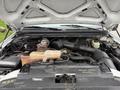 The image shows the engine compartment of a 2000 Ford F-450 with visible components like the battery coolant reservoir and various pipes and tubes