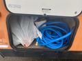 A 2015 Winnebago Of Indiana Travel Trailer storage compartment filled with a blue water hose a white trash bag and various other items