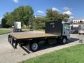 A 2015 Isuzu NPR flatbed truck with a wooden platform and a black metal cab guard positioned on a paved area